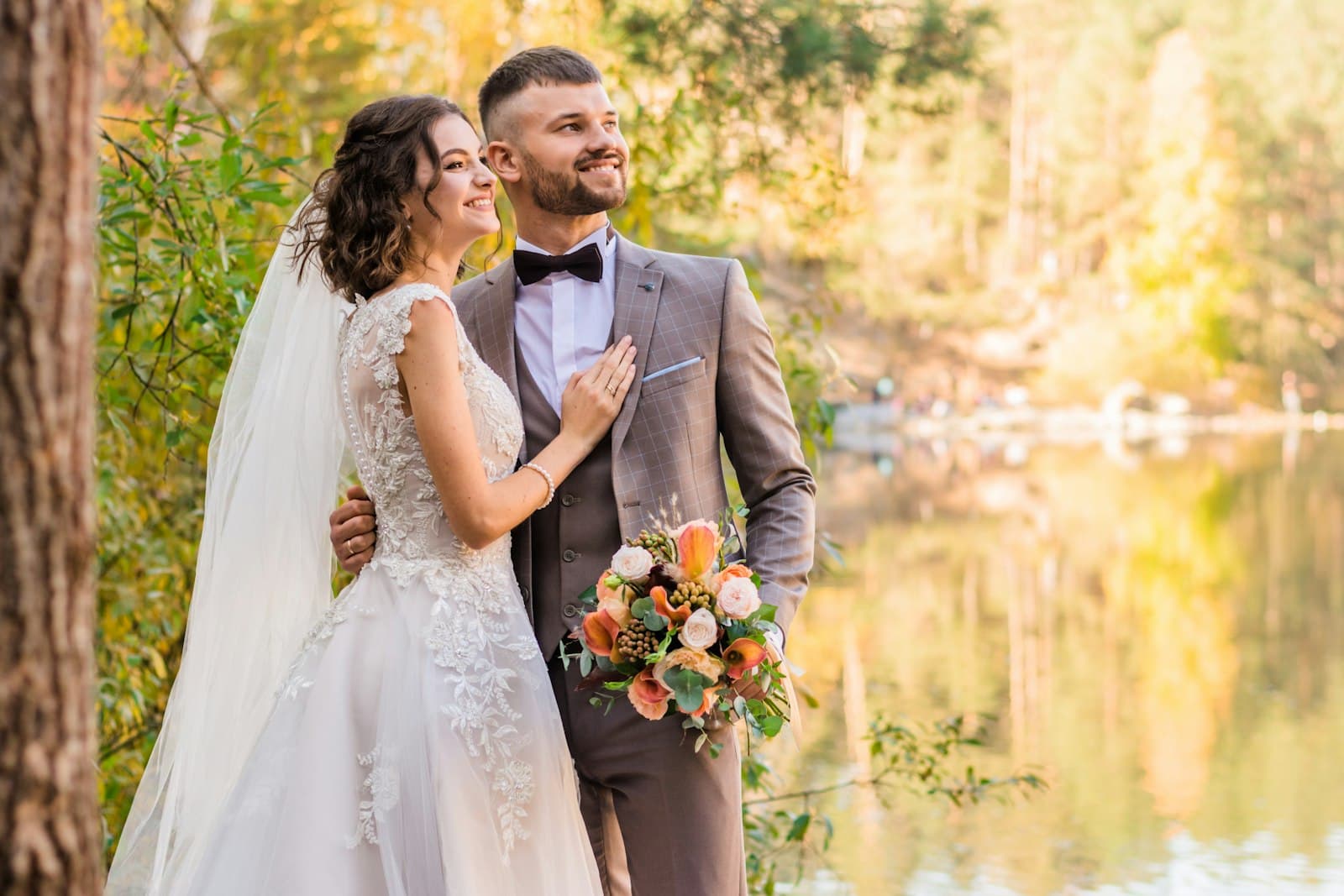 Bride and groom smiling by a lake in autumn light