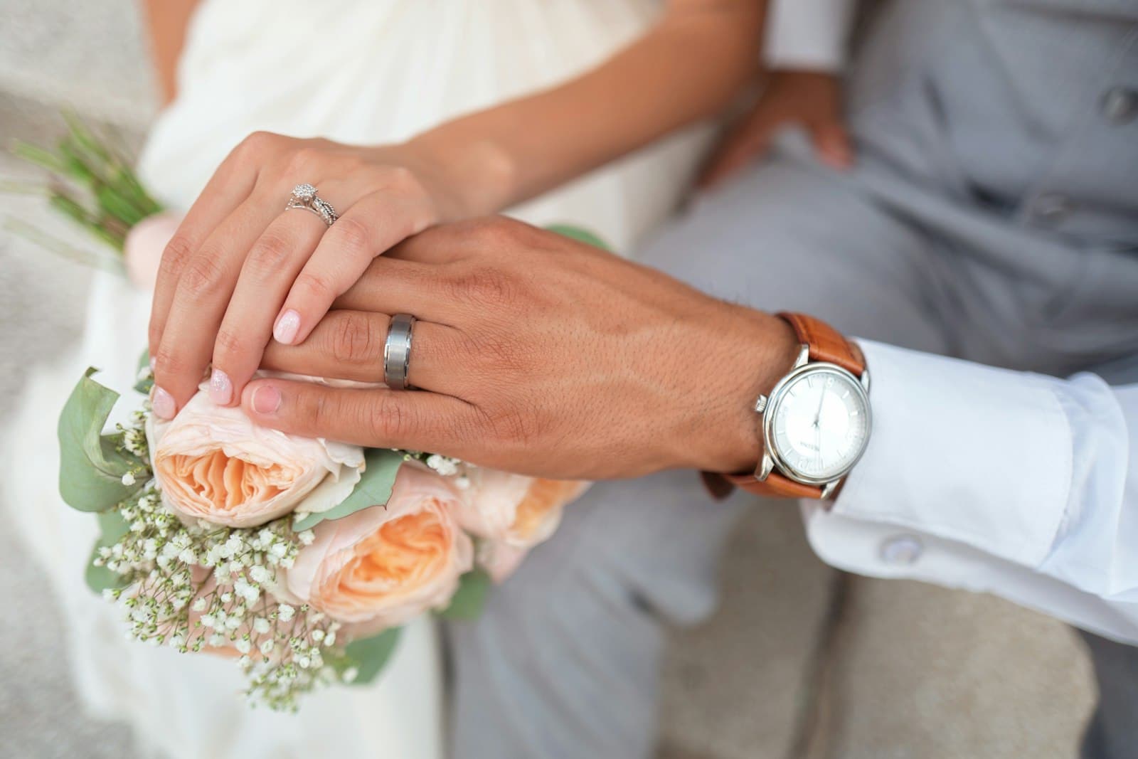 Couple’s hands with rings over a peach rose bouquet